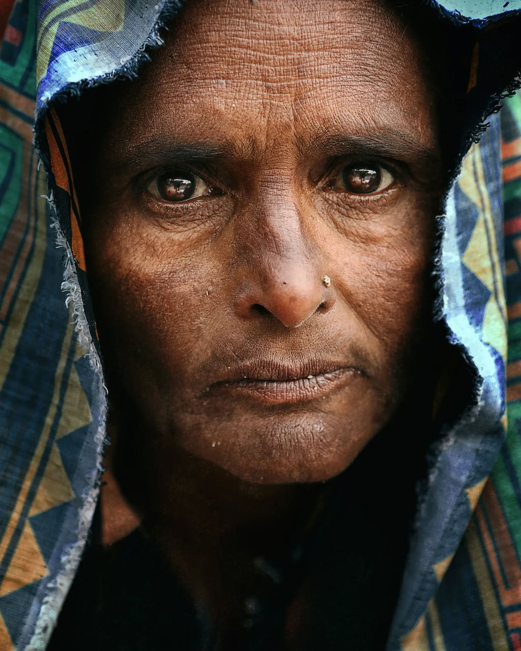 Close-up portrait of an African woman with deep-set eyes and a colorful head wrap