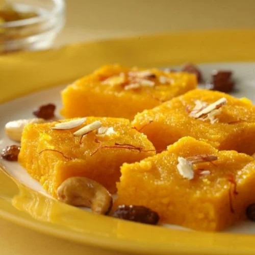 Golden yellow halwa pieces garnished with almonds and raisins on white plate