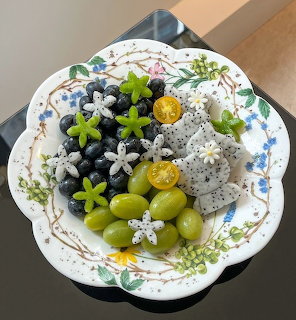 White decorative plate filled with fresh berries, grapes, dragon fruit and edible flowers on wooden surface