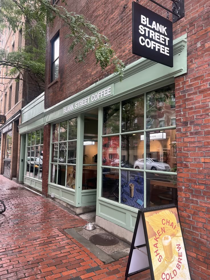 Blank Street Coffee storefront with sage green facade and hanging sign on a brick city street
