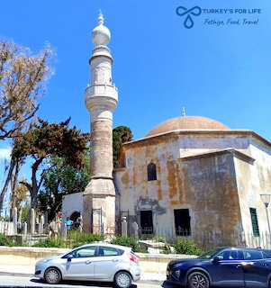 Old mosque with a tall minaret under a blue sky, with parked cars in front