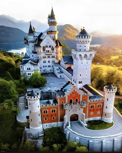 Neuschwanstein Castle on forested hilltop with mountains and sunset sky