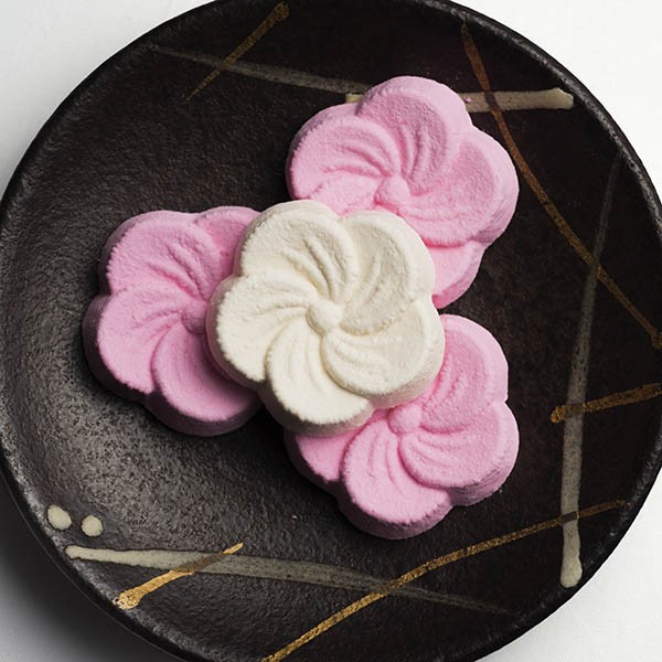 Pink and white Japanese wagashi sweets with spiral patterns on black plate