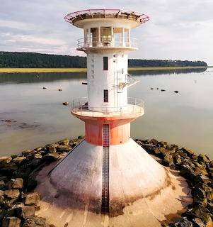 White cylindrical lighthouse with viewing platform on water surrounded by rocks