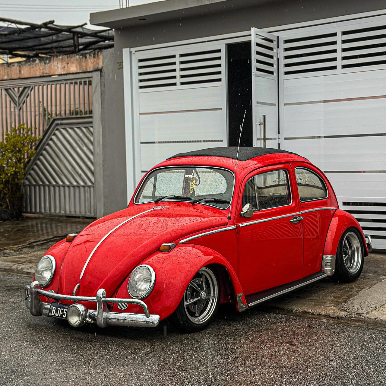 Red classic Volkswagen Beetle parked on a wet driveway outside a white garage