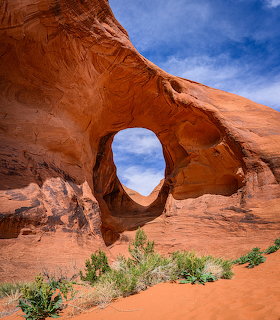 Natural sandstone arch in a red desert landscape with shrubs and blue sky