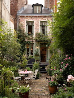 Brick townhouse with ivy-covered facade and lush courtyard garden with cobblestone path and pink roses