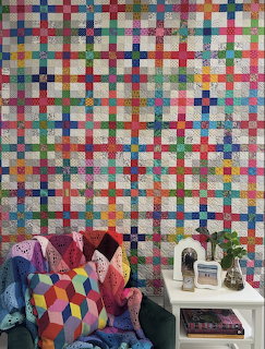 Colorful patchwork quilt with geometric pattern in bright squares displayed above a white sewing table