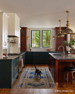 Modern kitchen with green island cabinets, dark countertops, brass fixtures, and natural light from garden-view windows