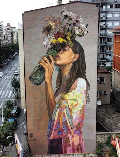Street art mural of a woman drinking from a bottle with flowers on her head, painted on a building in Belgrade