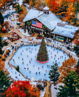 Aerial view of a snowy outdoor ice rink around a Christmas tree beside a rustic lodge
