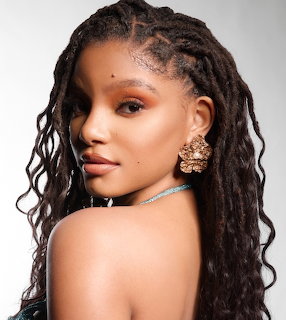Portrait of woman with long dark locs and gold earrings looking over shoulder