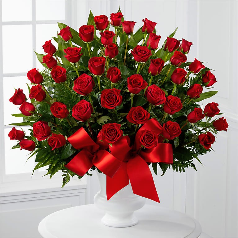 Large arrangement of red roses with green leaves and red bow in white vase