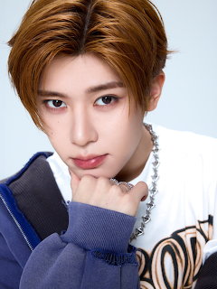Young male K-pop idol with orange hair posing with hand on chin wearing white shirt and blue jacket