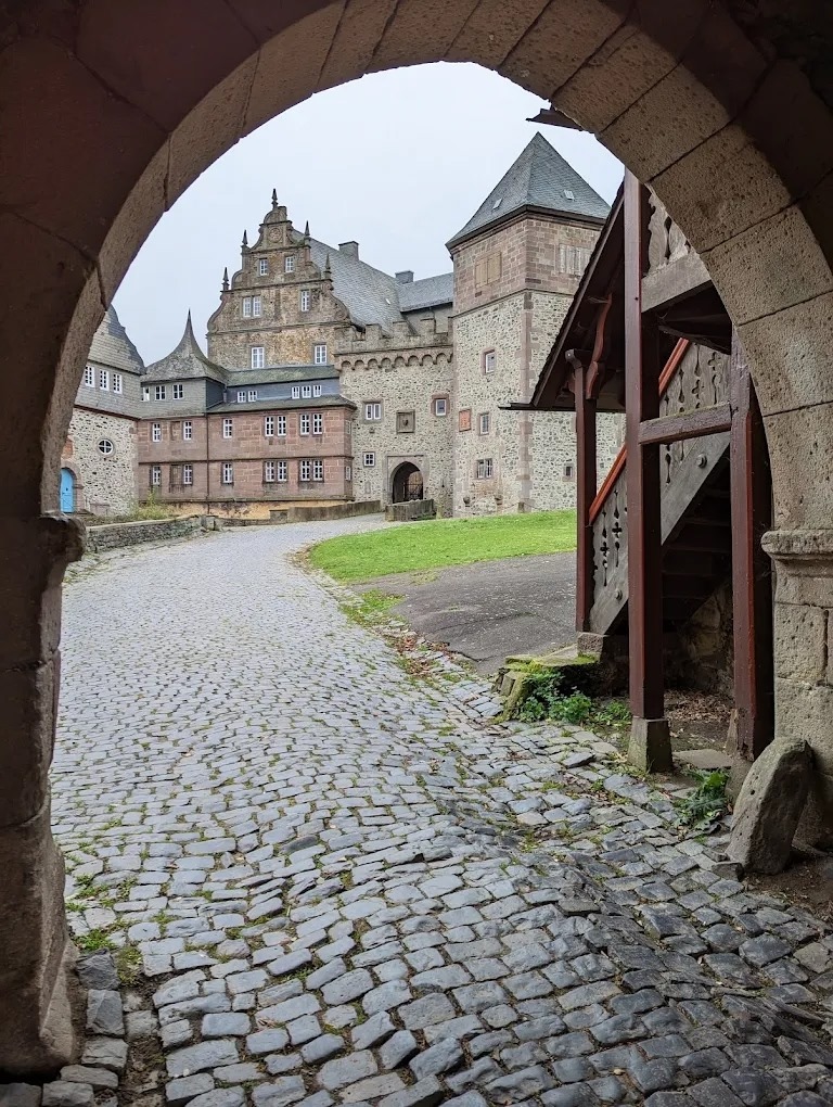 Stone arch framing a cobblestone castle courtyard with old buildings