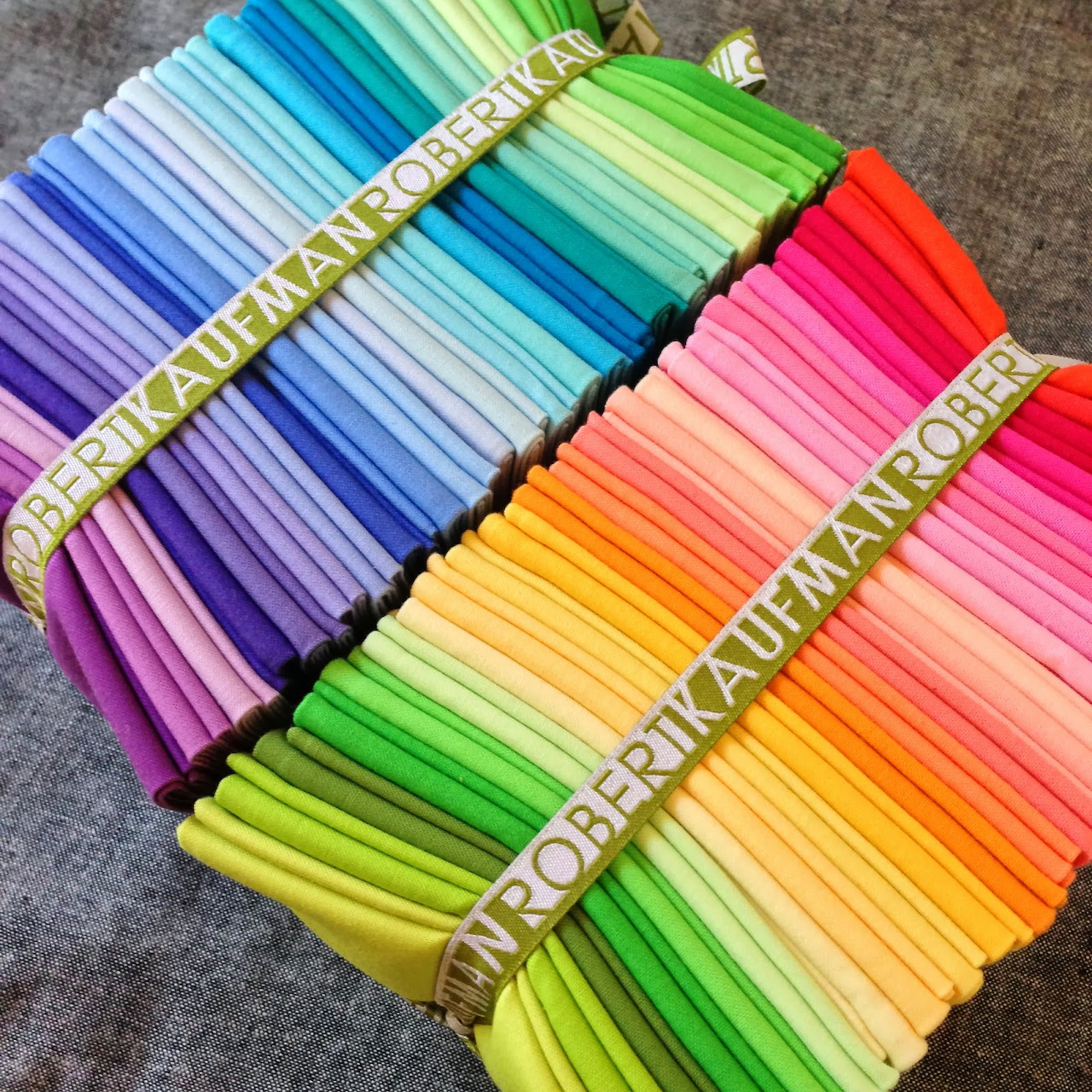 Rainbow spectrum of rolled fabric arranged diagonally with measuring tape across them