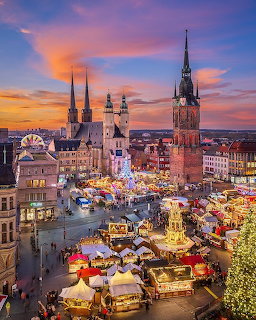Christmas market in Halle with lit stalls and church towers under a colorful sunset sky