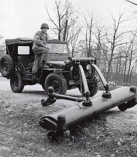 Soldier standing next to a military jeep with mine detection equipment mounted on the front