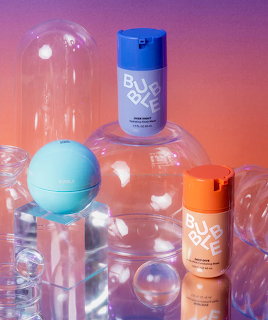 Blue and orange skincare bottles with light blue sphere among clear bubbles on gradient background