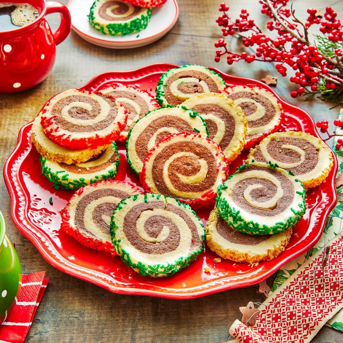 Colorful Christmas pinwheel cookies with spiral pattern on red plate surrounded by holiday decorations