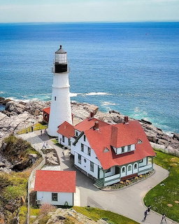 Aerial view of Portland Head Lighthouse with white tower and red-roofed building on rocky coastline