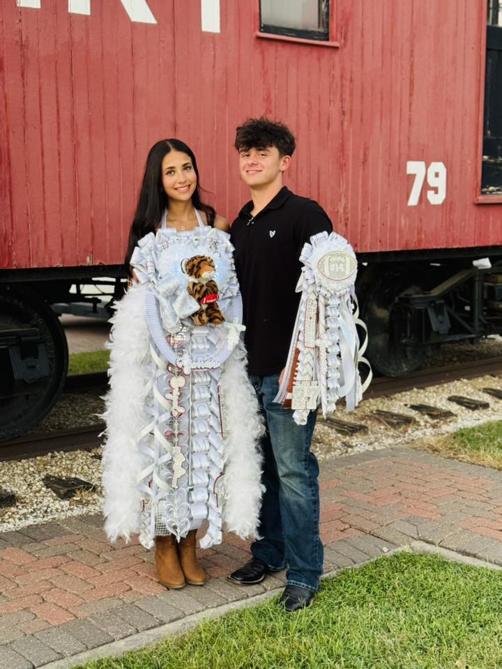 Teen boy and girl in formal wear with oversized white homecoming mums posing by red caboose