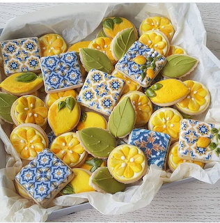 Assorted lemon-shaped and floral decorated cookies with yellow and blue icing on white parchment paper