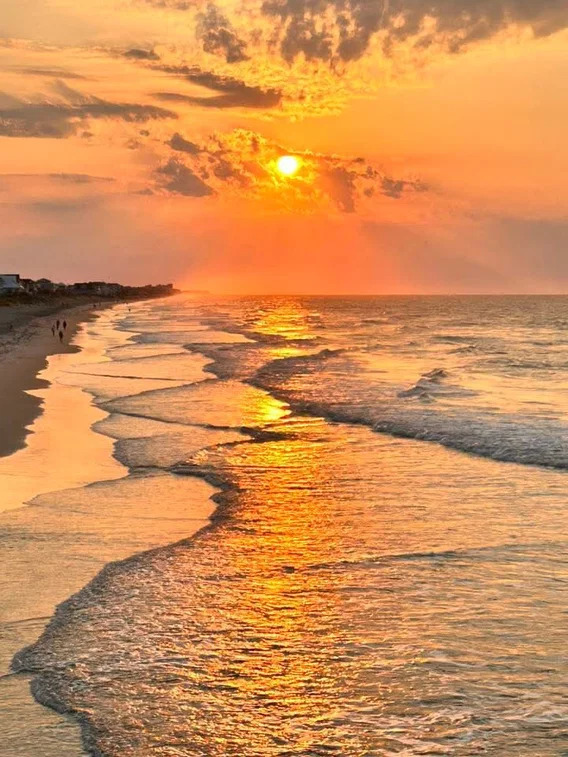 Golden sunset over a beach with rolling waves reflecting orange light on wet sand