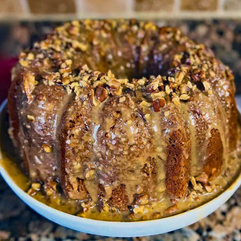 Glazed pecan bundt cake on a white plate with caramel dripping down the sides