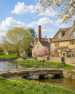 Cotswold stone cottages with a stone bridge over a stream surrounded by spring blossoms