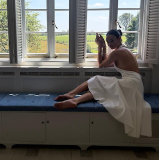 Woman in white dress sitting on window sill looking outside