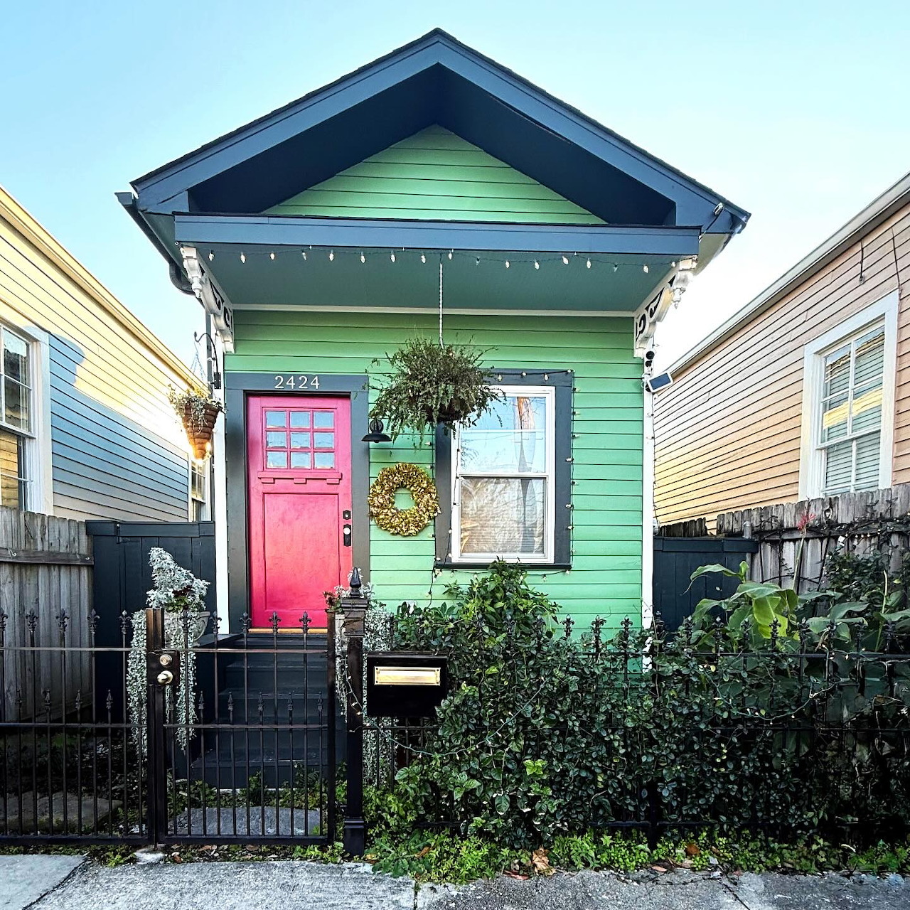 Small turquoise house with pink door and hanging plants between two neighboring homes