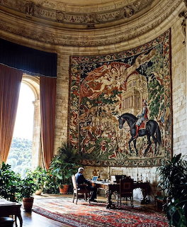 Large equestrian tapestry on curved wall in a grand castle room with arched window and desk