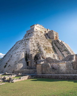 Pyramid of the Magician at Uxmalayan ruins with green lawn and blue sky