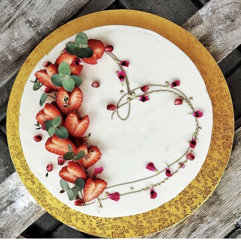 Top view of a white cake decorated with strawberries and small pink flowers on a gold plate