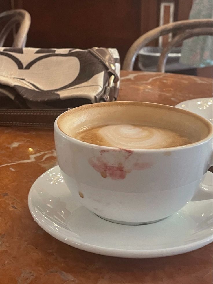 White cappuccino cup with a lipstick stain on a saucer on a brown café table