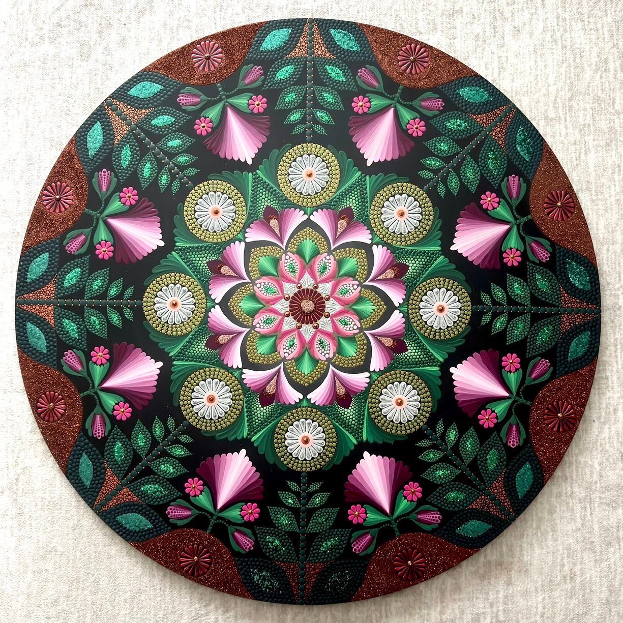 Circular mandala with symmetrical pink flowers, green leaves, and ornate gold medallions on textured background