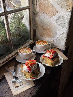 Two lattes and cake slices on plates by a rustic window