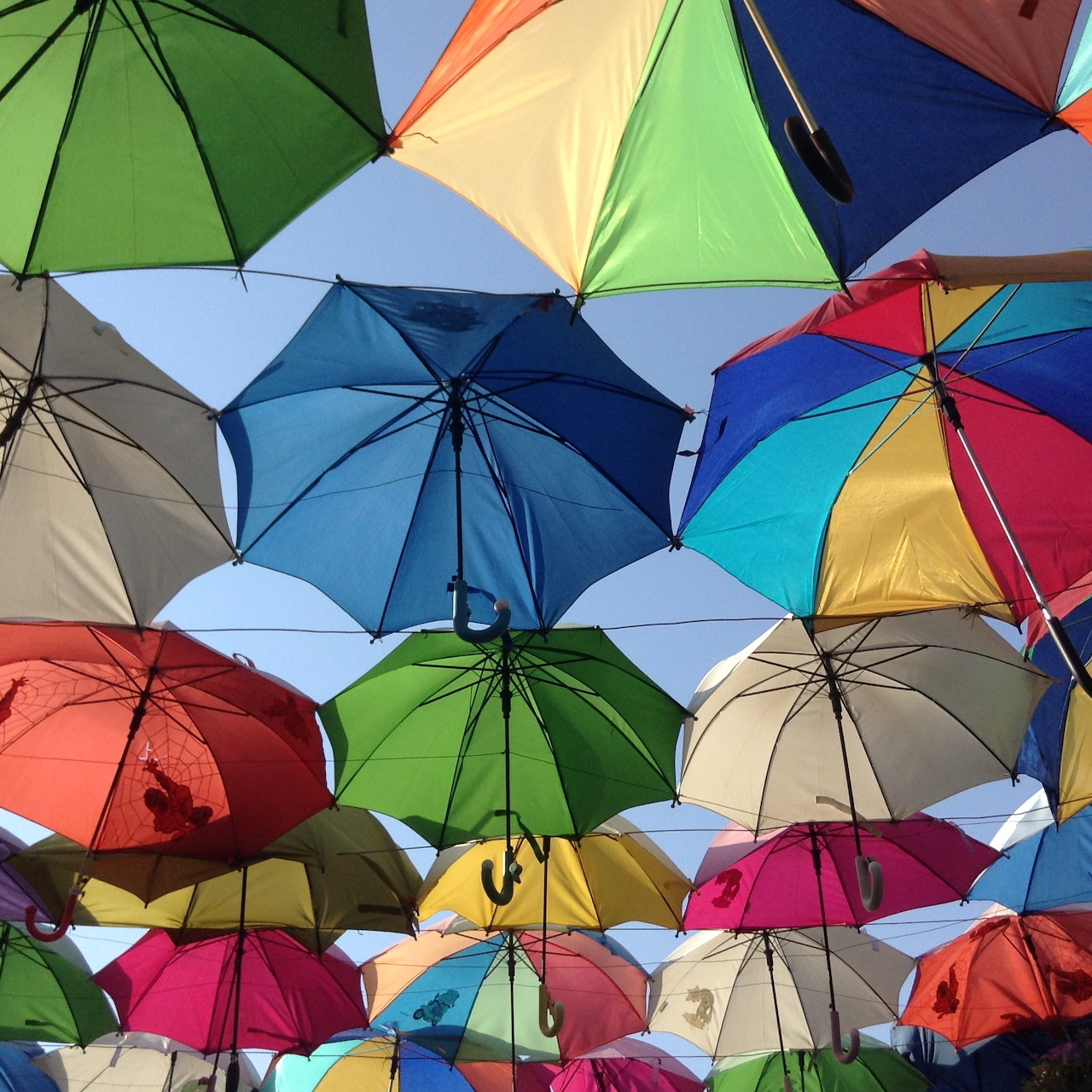 Colorful umbrellas hanging in the sky creating an artistic installation with blue, green, yellow, and pink parasols