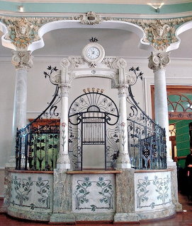Ornate Art Nouveau entrance hall with decorative ironwork, floral moldings, and painted botanical panels