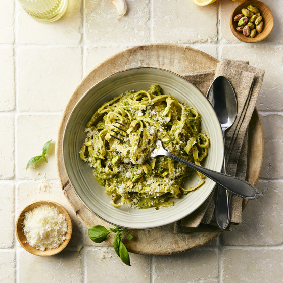 Bowl of penne pasta with pistachio pesto and grated cheese on white tiles