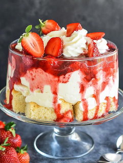 Layered strawberry cheesecake trifle with fresh strawberries and cream in glass pedestal bowl