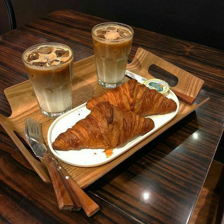 Two iced coffee drinks and croissants on wooden serving tray