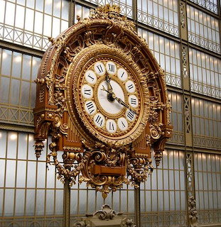 Ornate antique clock with Roman numerals in front of tall glass and metal walls