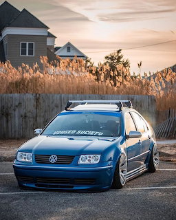 Lowered blue Volkswagen Bora sedan parked outdoors near a fence and houses