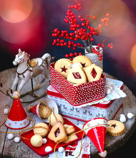 Christmas cookie display with polka dot tin, star cookies, toy horse, red berries and Santa hat on wood table