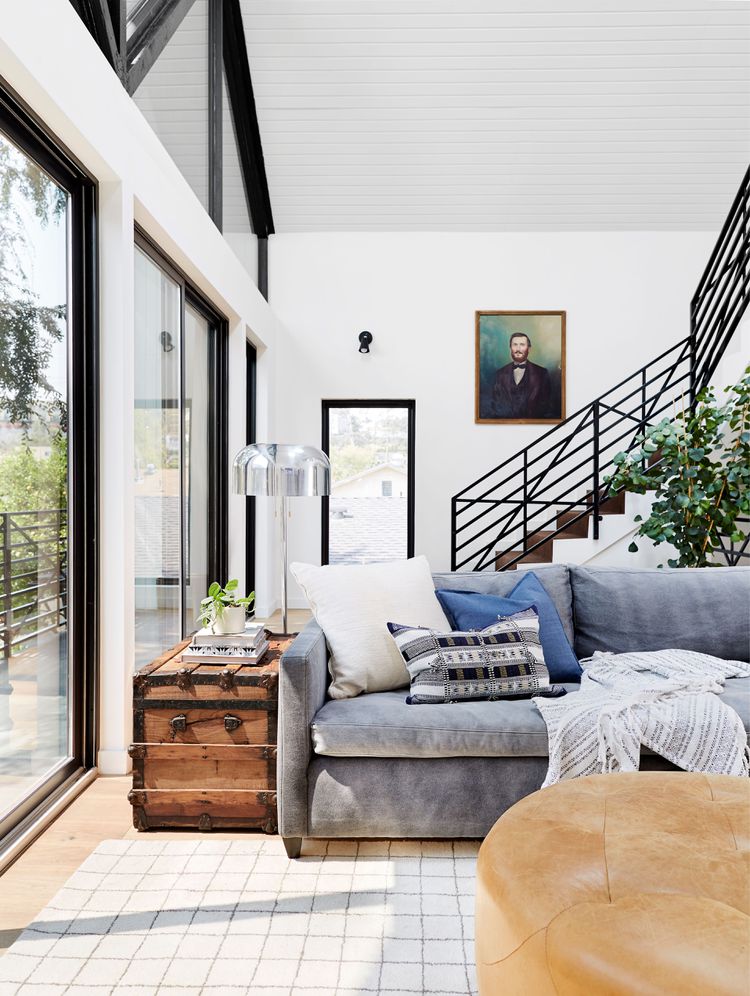 Modern living room with gray sofa, pendant lights, staircase, and large windows