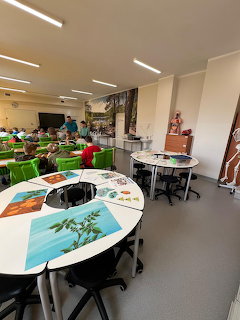 Modern school classroom with round tables, green tablecloths, and young students working on activities