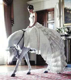 Woman in a flowing white gown beside a white horse in an elegant indoor room