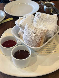 Basket of beignets covered in powdered sugar with two small cups of dipping sauce on a white plate